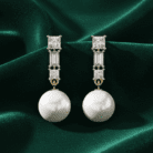 Planet Genesis - Pearl drop earrings with large round pearls, rectangular and square diamonds in gold, displayed on green satin fabric. Premium design. - IGI-Certified Lab-Grown Diamonds