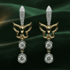 Planet Genesis - Gold butterfly earrings with diamond accents and two round dangling gemstones each, displayed on dark green velvet fabric. - IGI-Certified Lab-Grown Diamonds